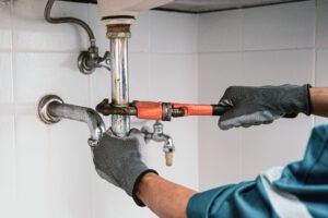 Plumber using a wrench to repair water pipe under the sink.