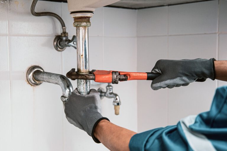 Plumber using a wrench to repair water pipe under the sink.